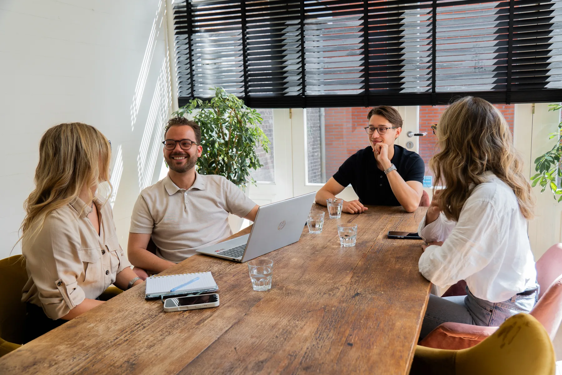 Vier mensen in overleg aan een houten tafel met een laptop